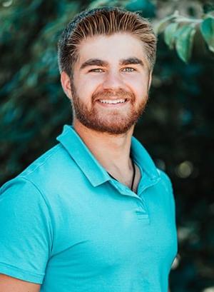 Image of Wyatt Sharkey wewaring a blue polo shirt smiling at the camera. 