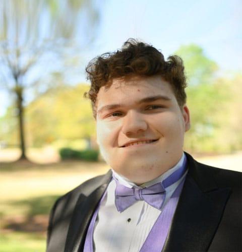 John Daniel from South Carolina Connections Academy in a black suit and purple bow tie outside on a sunny day.